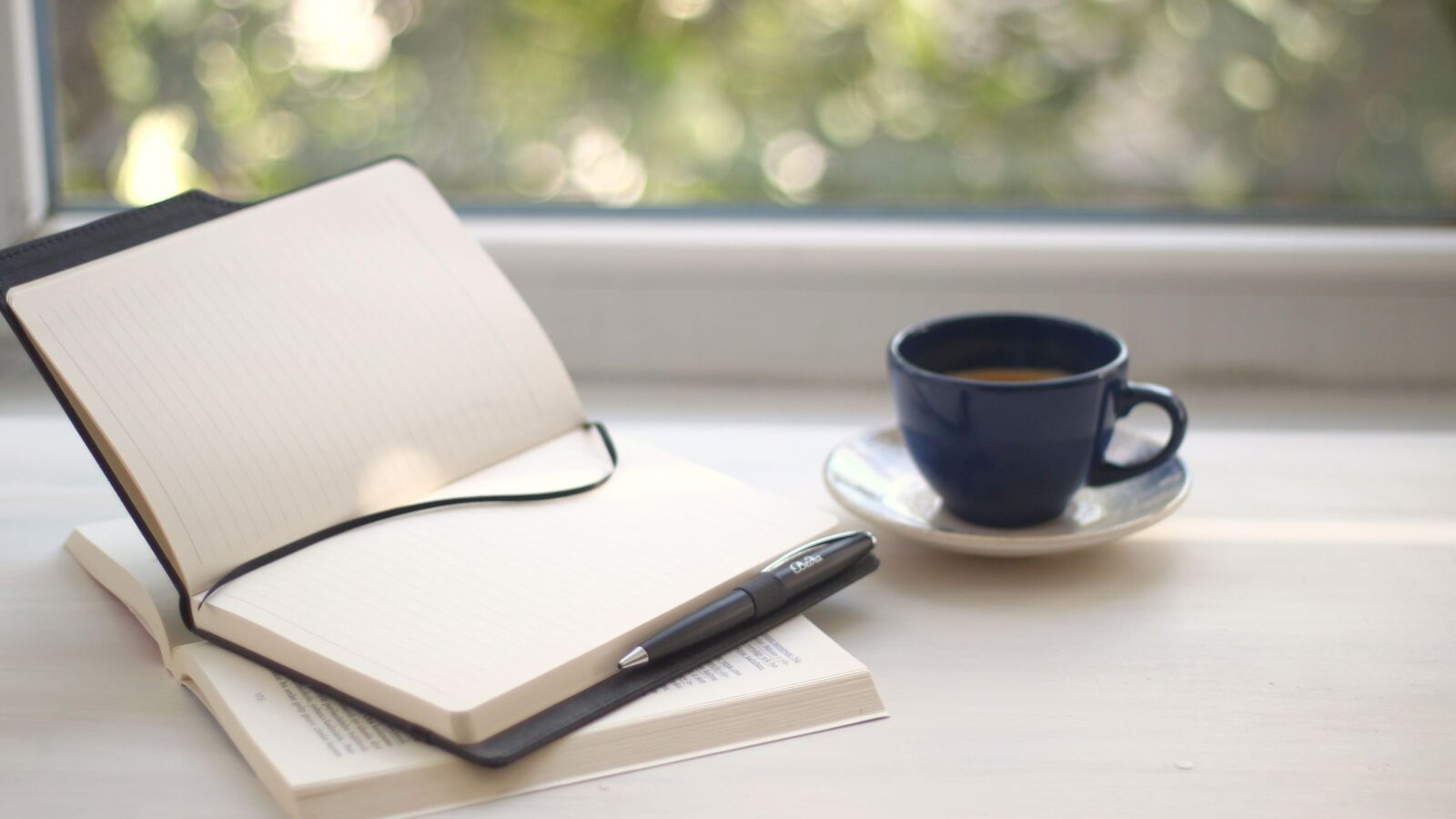An open notebook and a cup of coffee on a windowsill