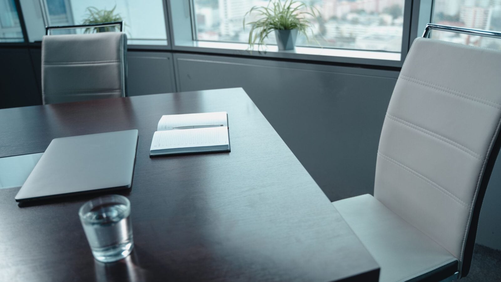 A quiet meeting table by a window with a glass of water and a notebook