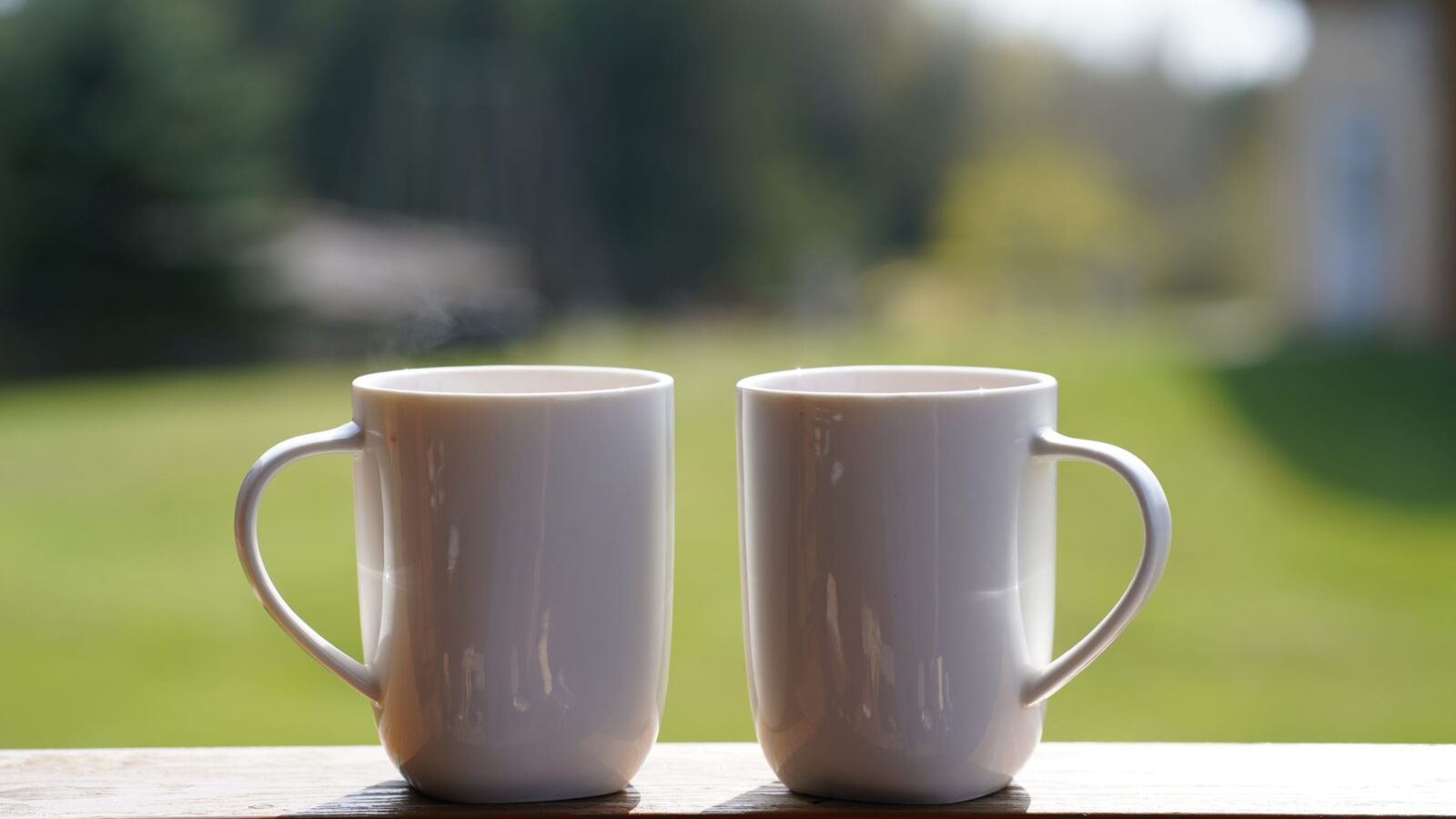 Two white mugs side by side on a porch rail