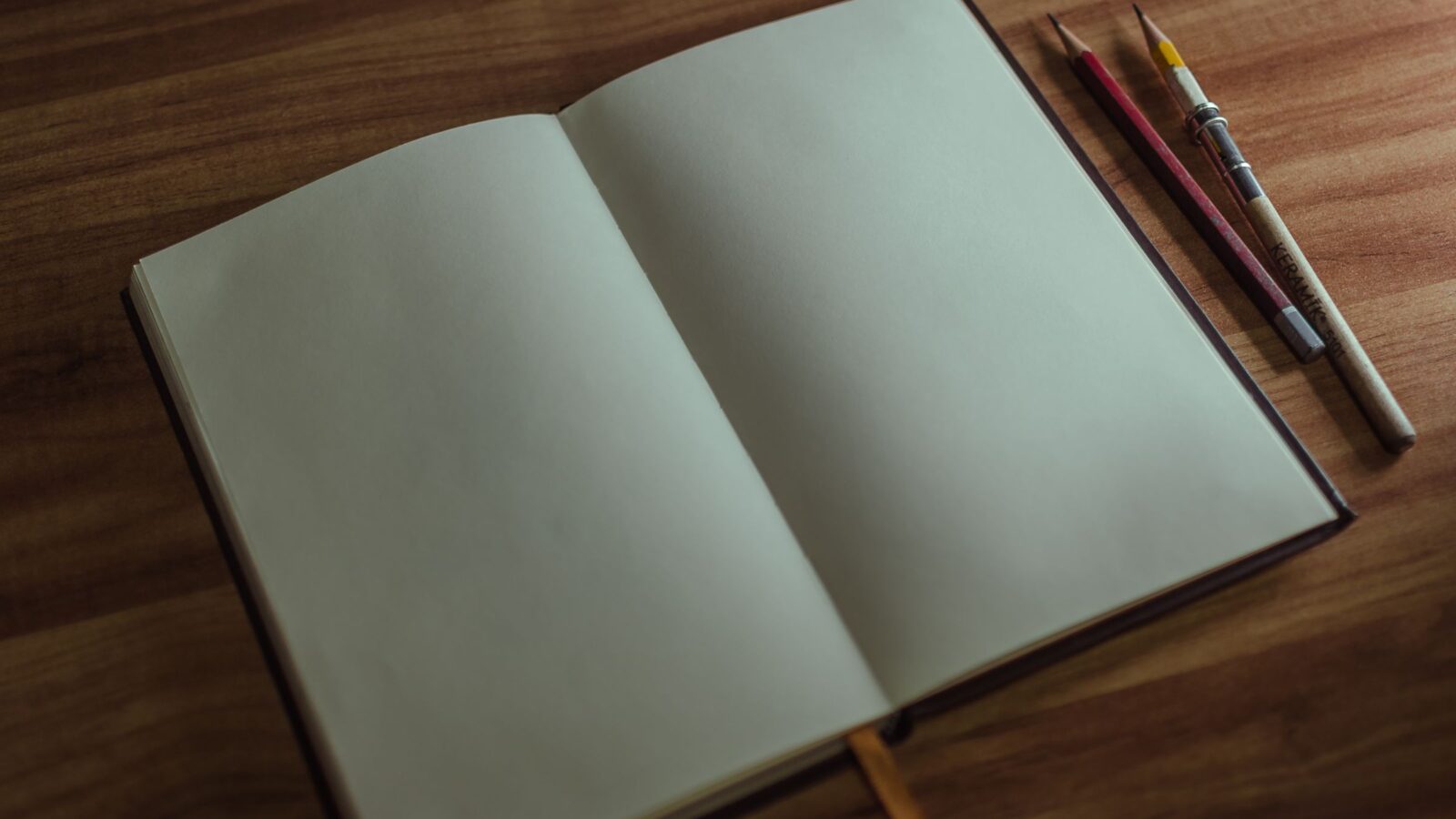 An open blank notebook with pencils on a wooden desk