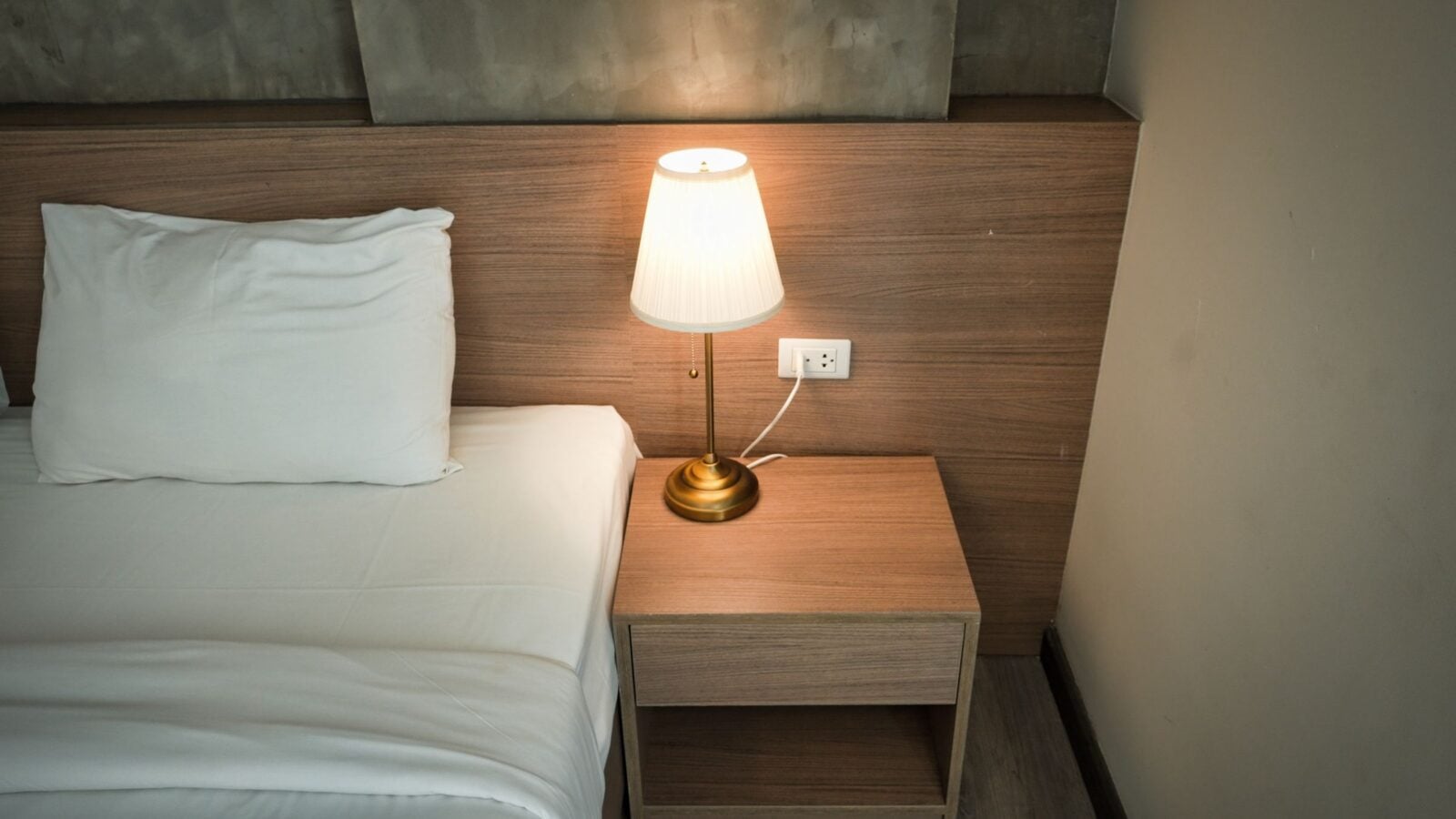 A bedside lamp glowing beside a made bed