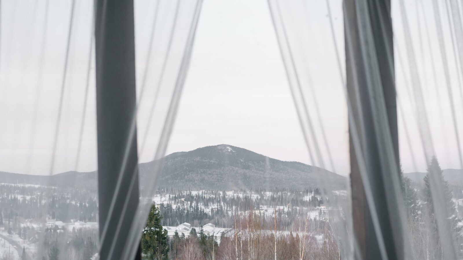 Sheer curtains open on a window with a view of snowy hills